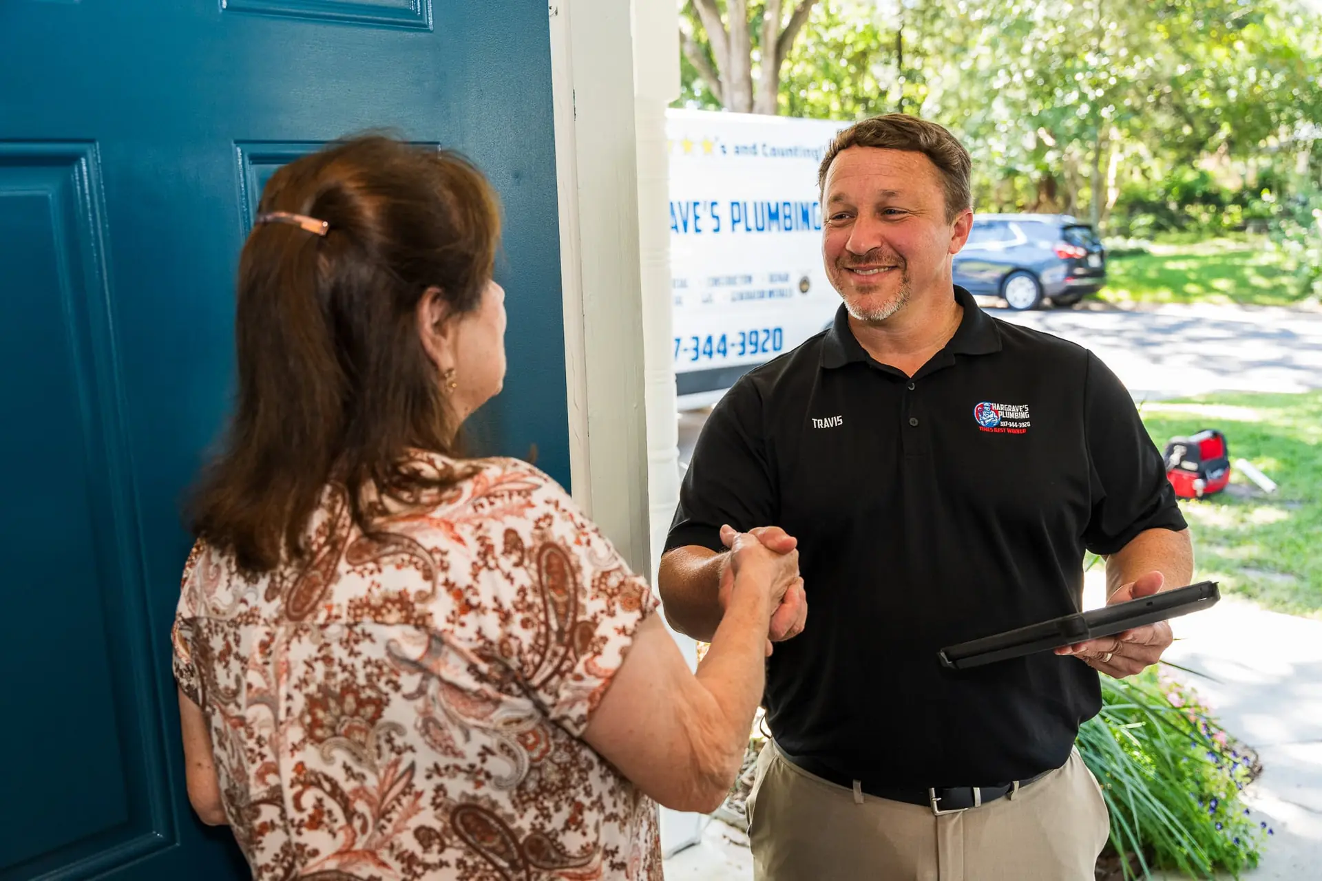 Hargrave's Plumbing greeting a customer at her door, service van at the curb