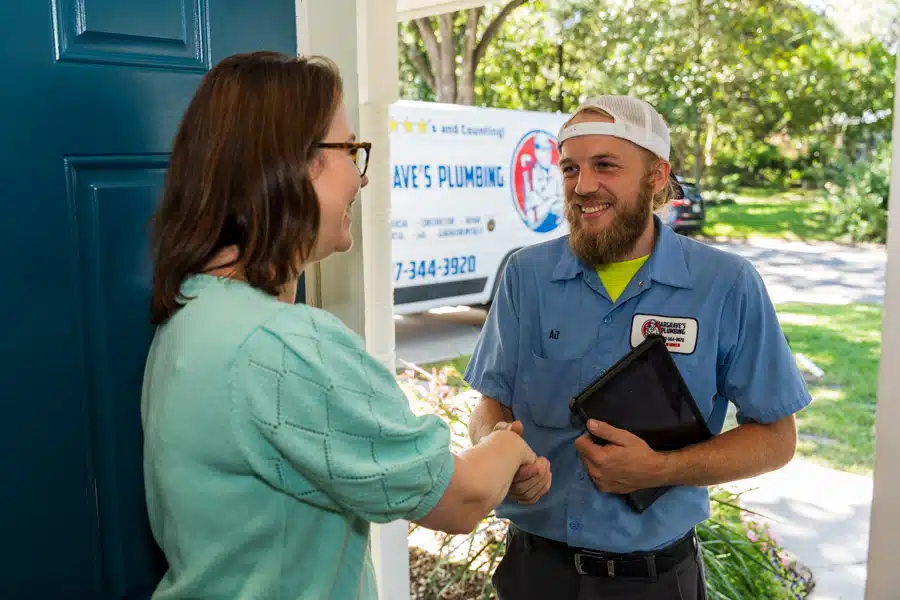 A Hargrave's Plumbing technician shaking hands with a customer at her front door, the branded service van at the curb behind him